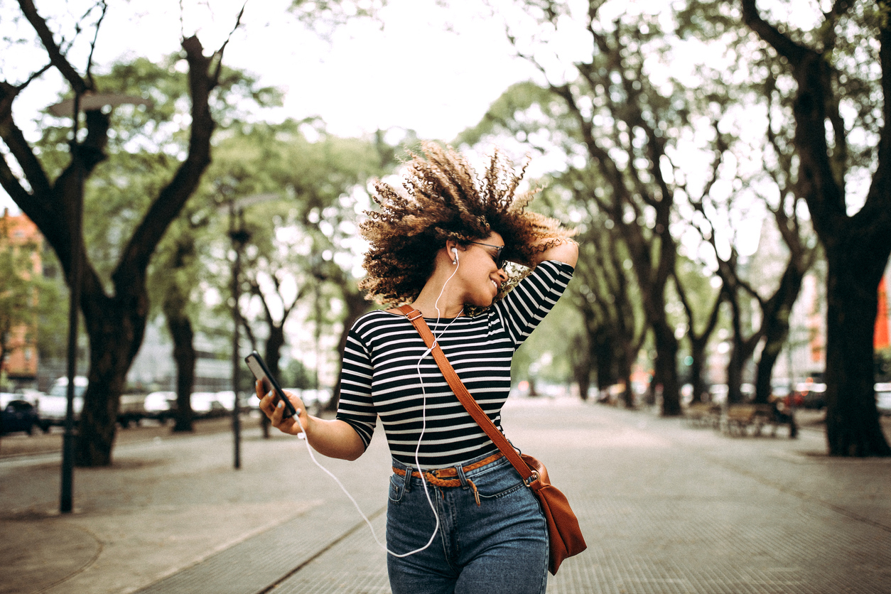 Happy woman listening to music and dancing on the street