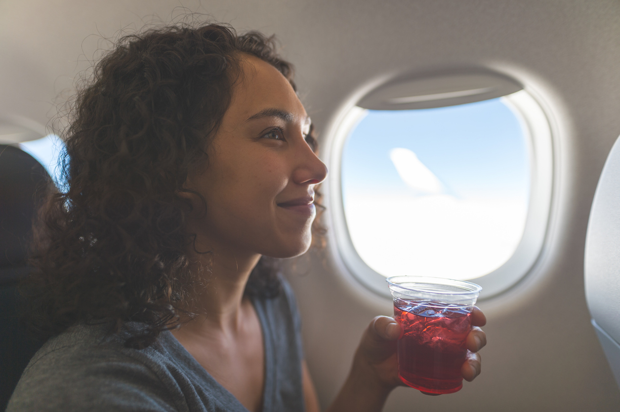 A woman drinking a beverage or cocktail on a flight