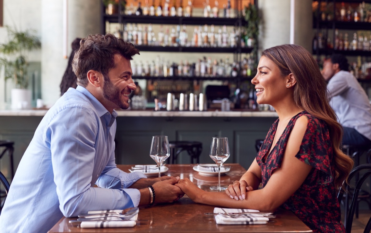 man and woman sitting across one another at a table holding hands