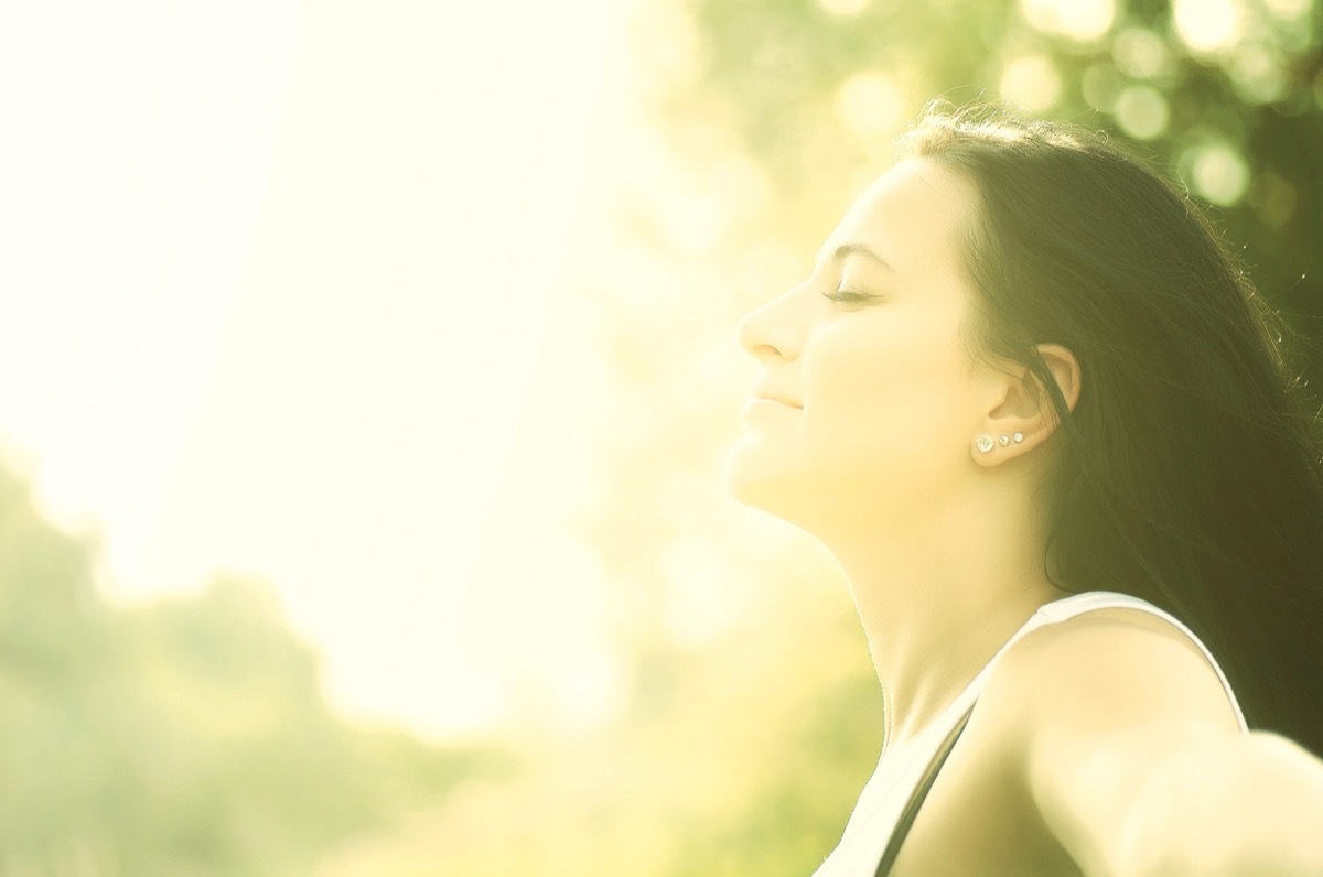 young woman enjoys sun beams at summer park.