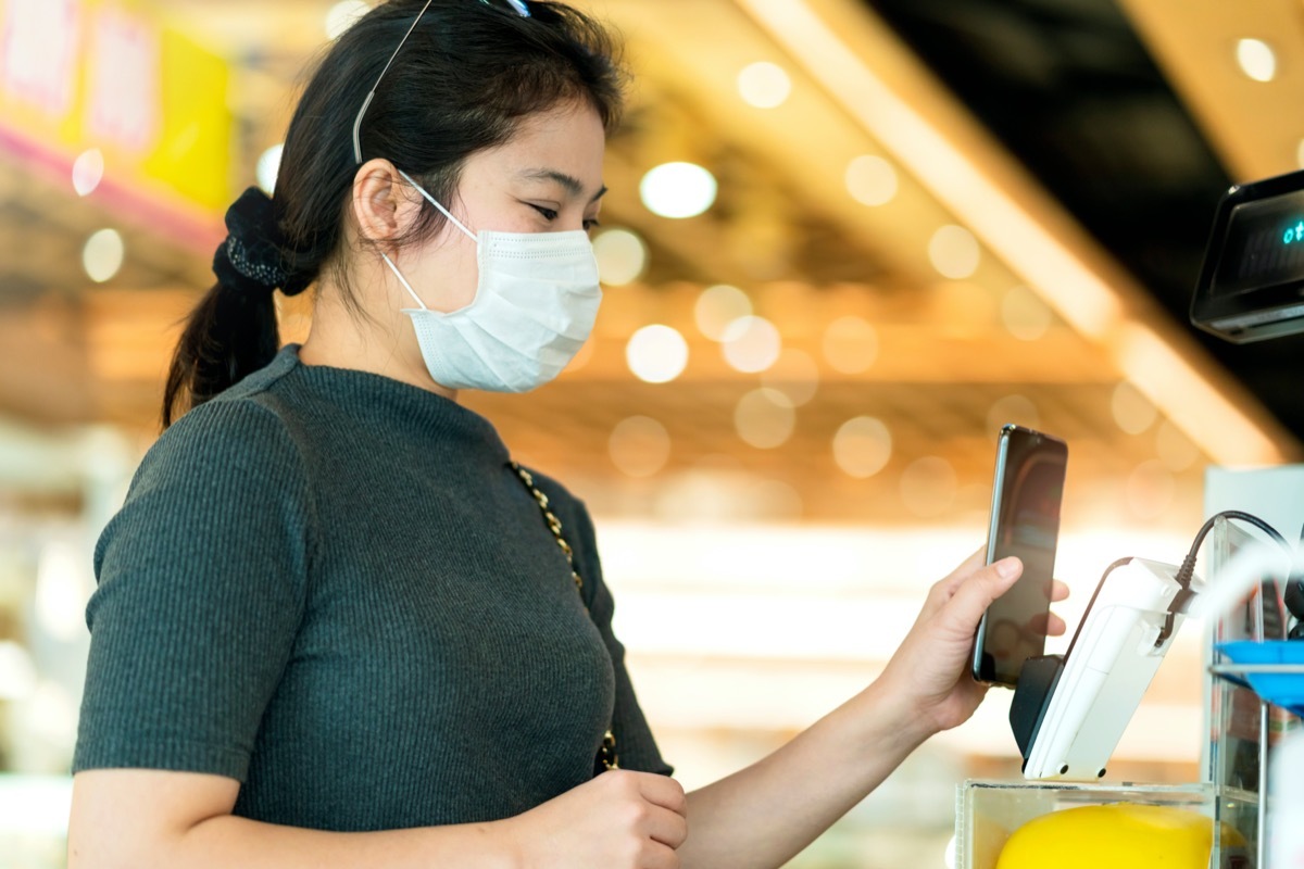 young asian woman in mask using phone to pay