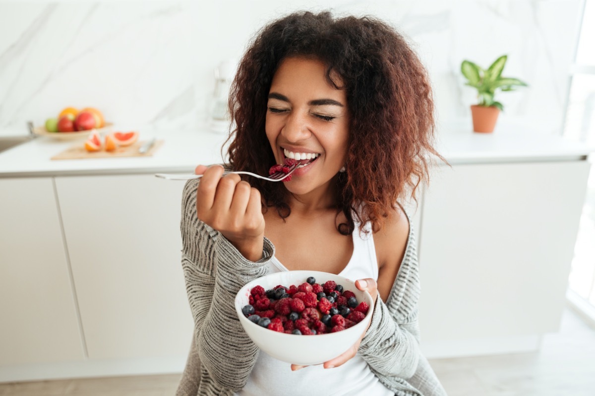 Young healthy laughing african woman eating breakfast and fruits in kitchen in the morning