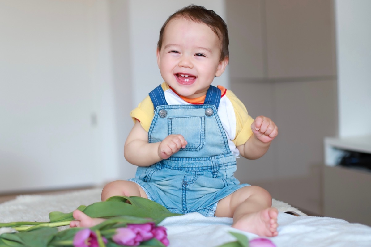 cute baby boy siting on bed next to a pile of tulips