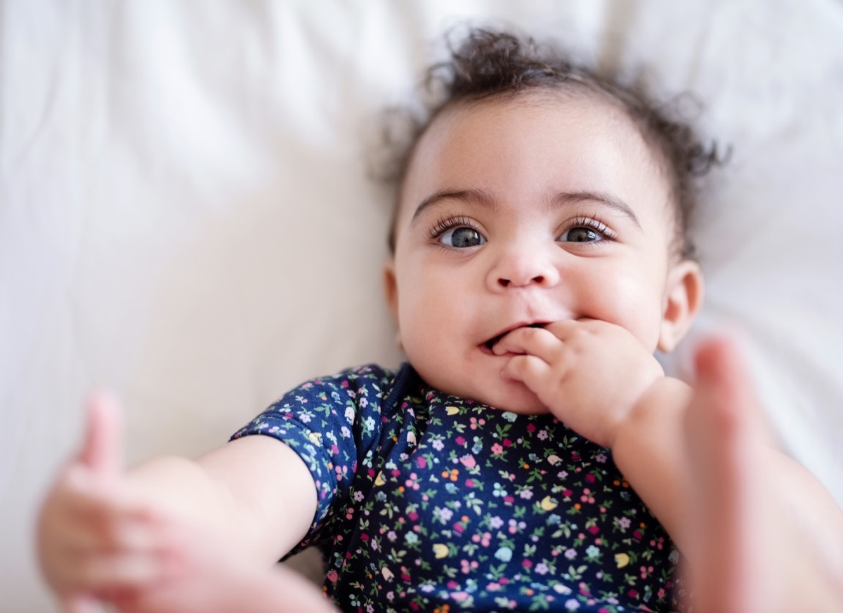 Shot from above of cute baby girl lying on bed and playing