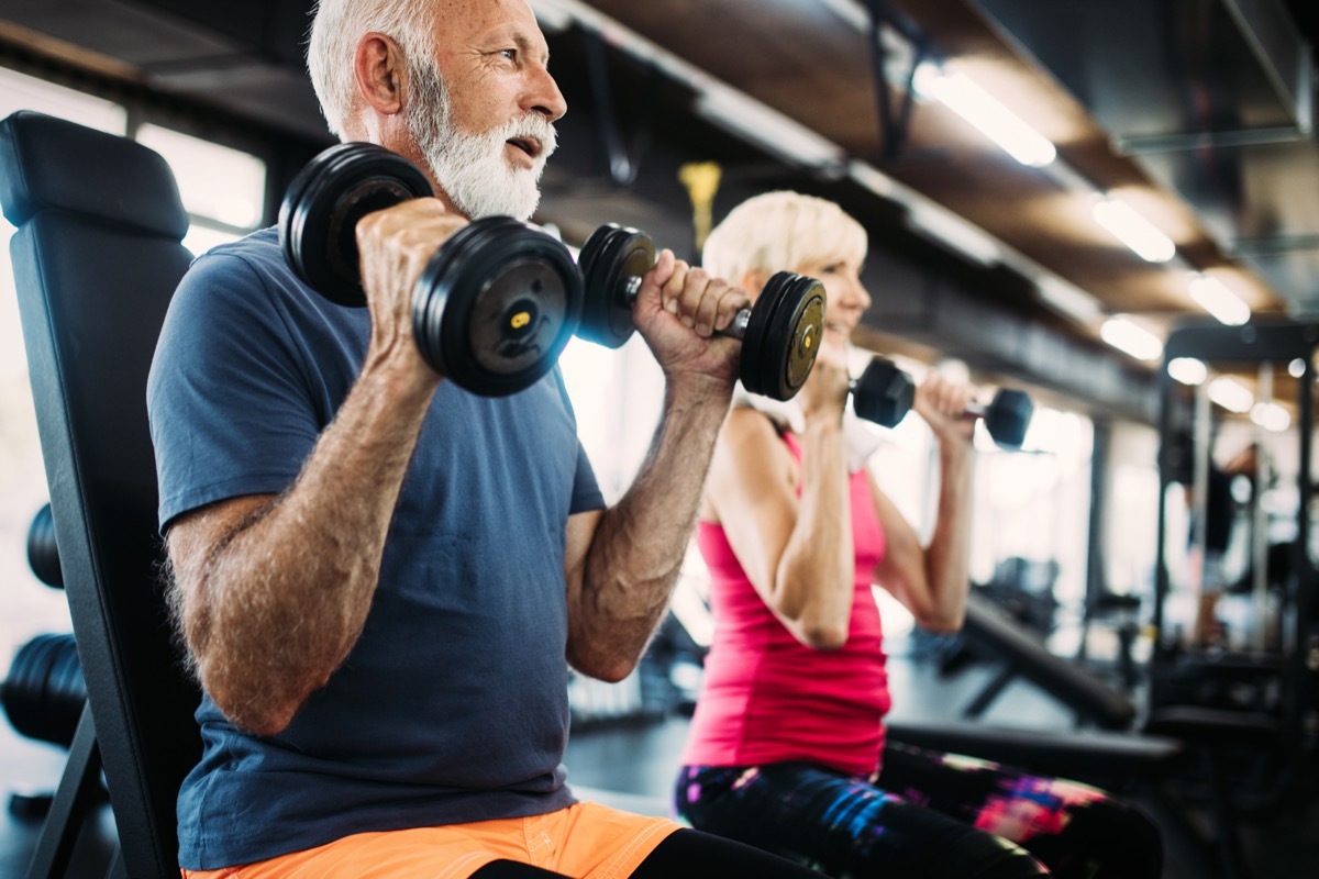 Older couple lifting weights working out at the gym