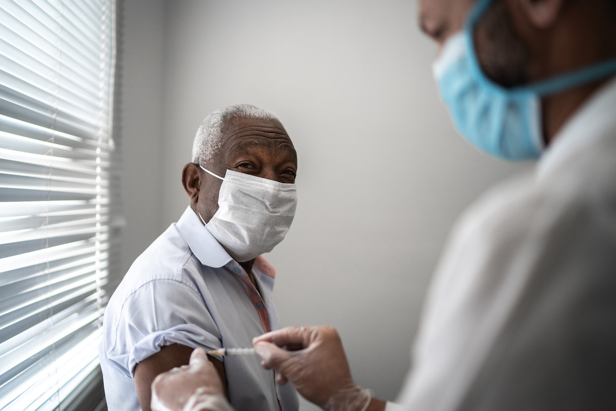 Nurse applying vaccine on patient's arm while wearing a face mask