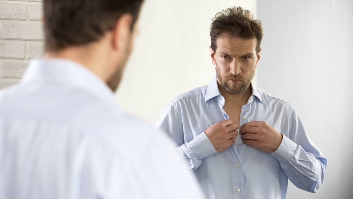 Sleepy man wearing shirt, preparing for work in morning, unhappy with appearance