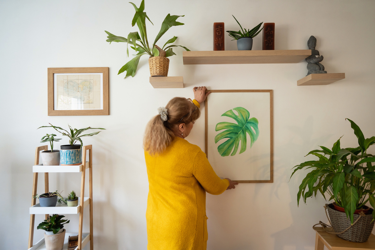 Senior Caucasian woman hanging a painting on the wall.