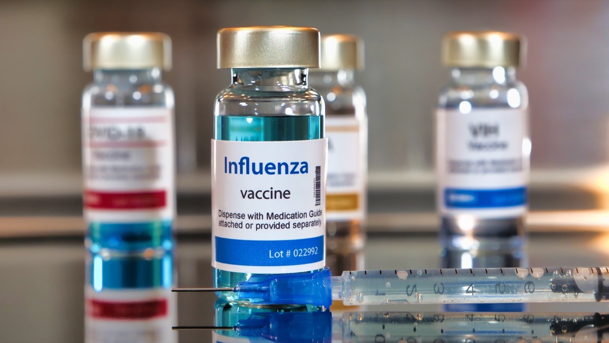 Vials of influenza vaccine. ottles with a syringe on black table and stainless steel background.