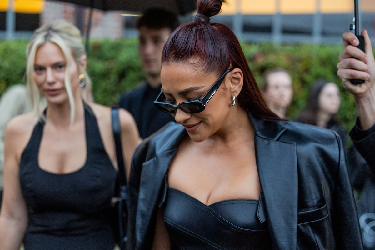 Shay Mitchell wears black cropped top and black leather blazer while looking down in sunglasses