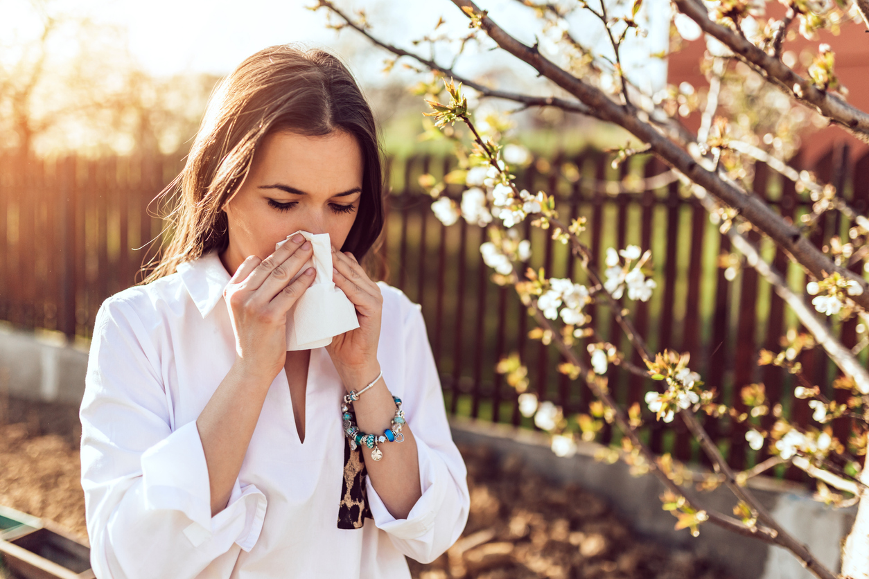 Woman sneezing into a tissue outdoors.