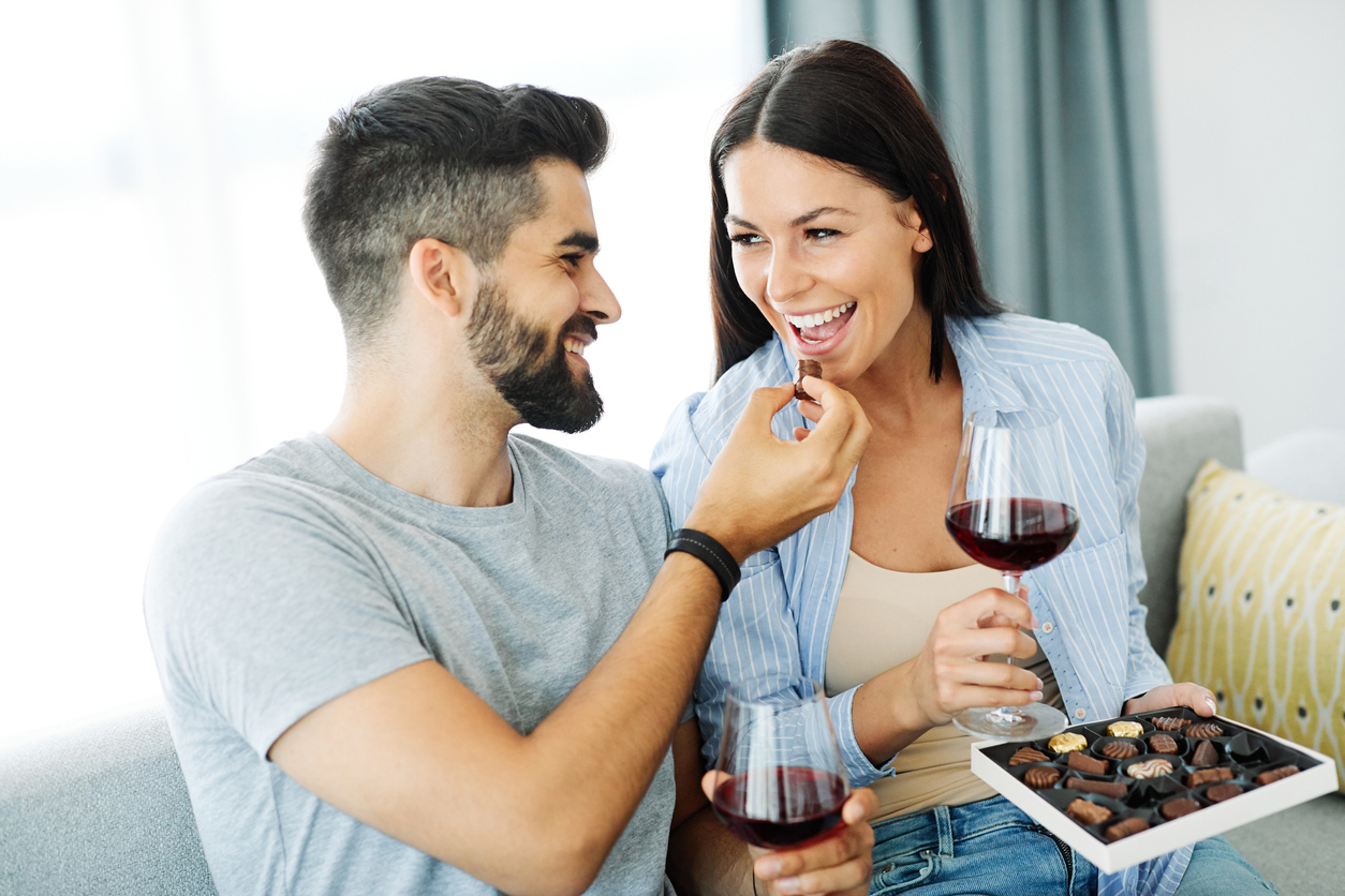 Portrait of a lovely young couple eating chocolate praline together on sofa at home