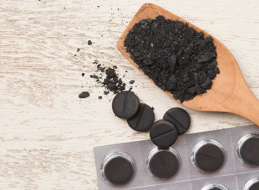 scoop of activated charcoal powder with charcoal tablets