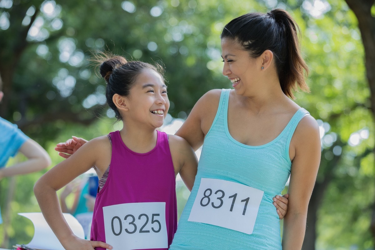 Asian mother and daughter pose together during a race in a public park on a sunny day.