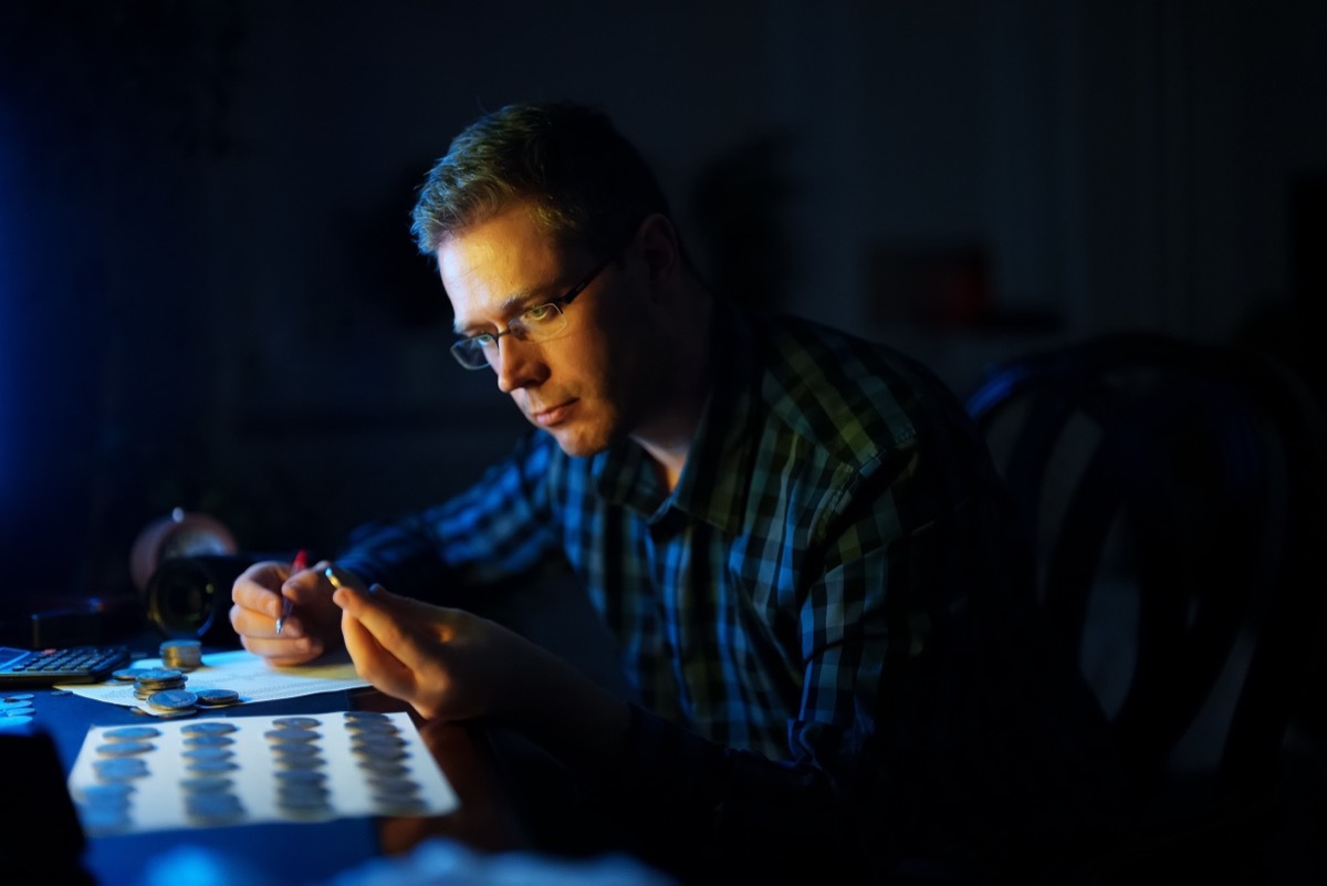 Male numismatist examines collection of coins.