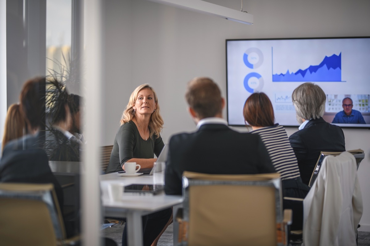 Rear view personal perspective of executive team video conferencing with male CEO and discussing data.