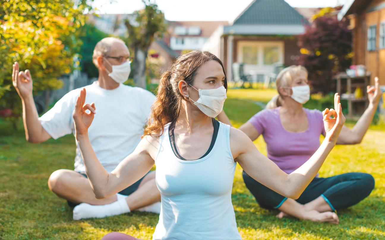 A group of mixed aged people do yoga outdoors with face masks on to stop the spread of COVID