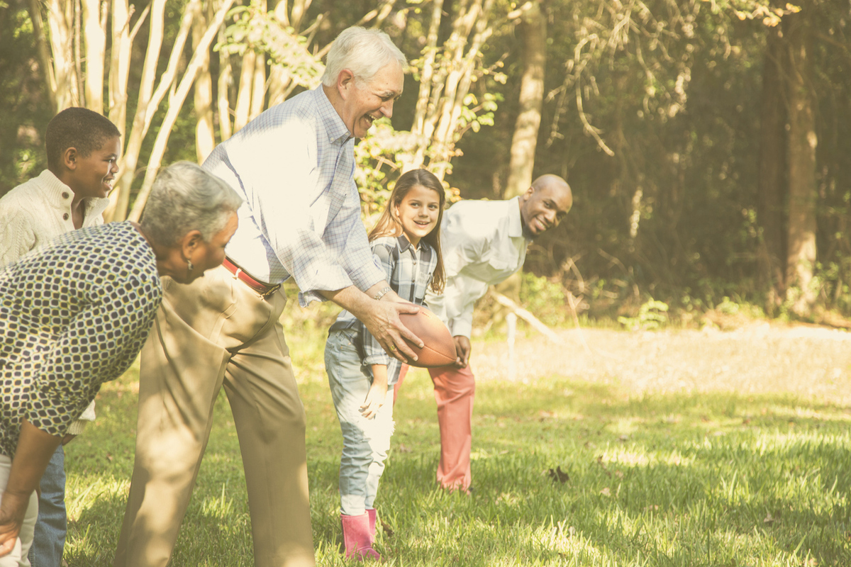 Multi-ethnic, multi-generation family members playing a football game together in grandparents' backyard on Thanksgiving Day