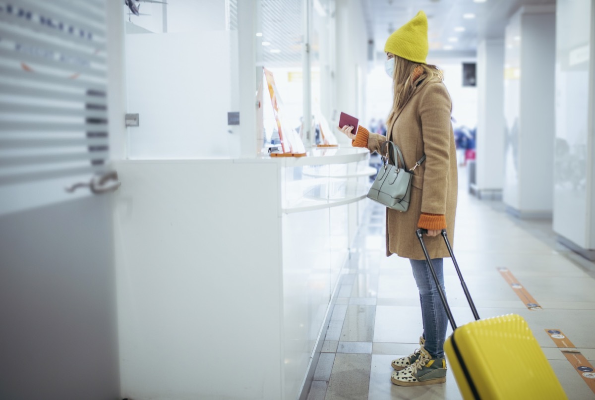 A young woman is at the airport's check out counter. She's waiting to leave the airport as soon as the customs officer checks on her passport.