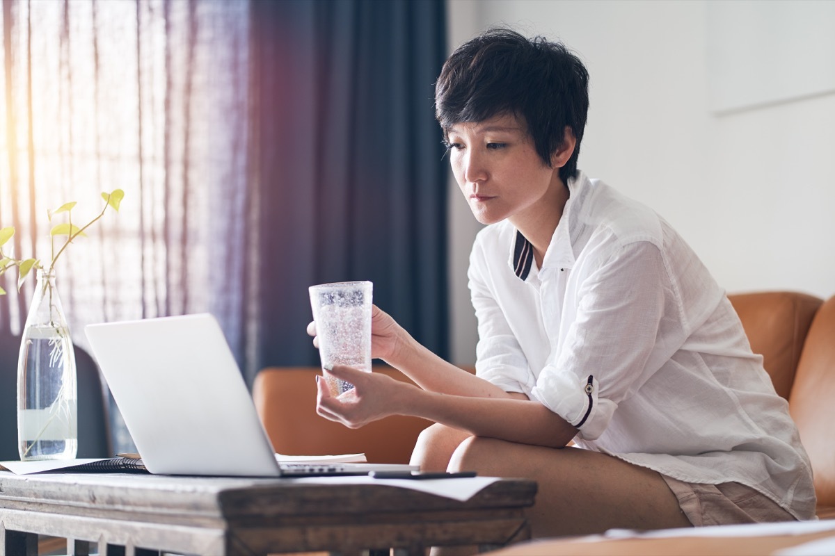 Asian woman drinking a glass of water on the couch unhealthy habits after 40