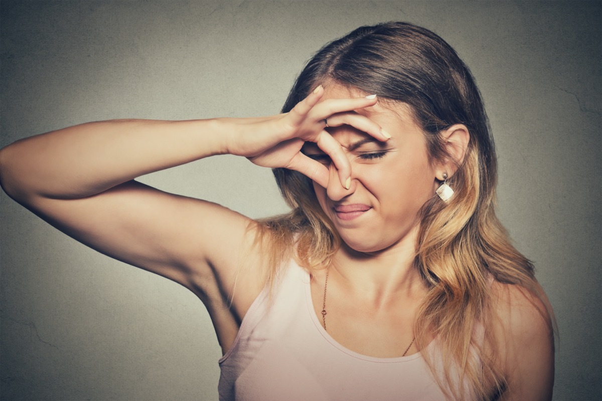 Closeup portrait headshot woman pinches nose with fingers hands looks with disgust