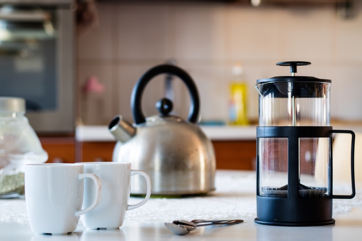 french press, silver kettle, and two white mugs on kitchen counter