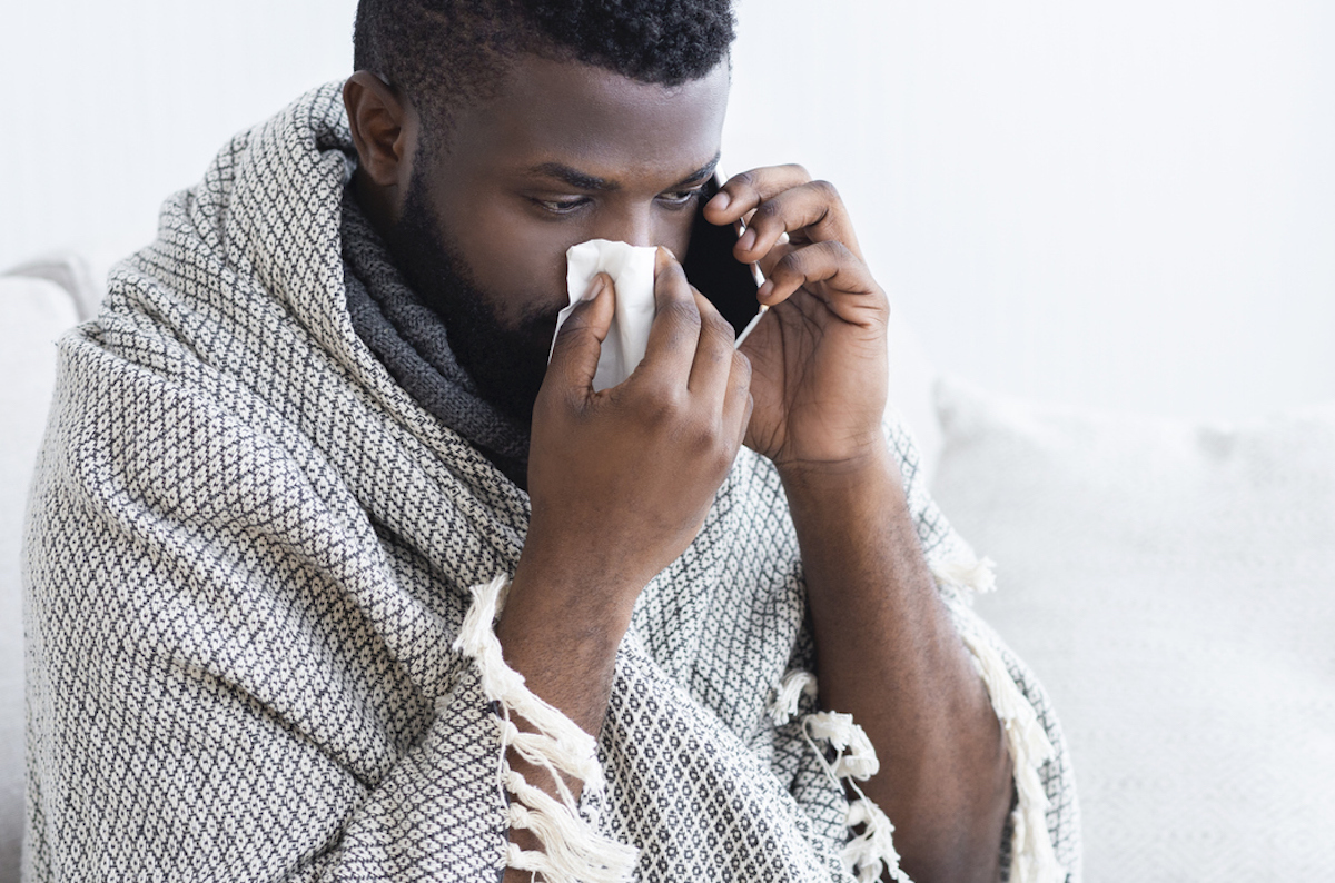 sick black man talking to doctor on phone while blowing his nowse