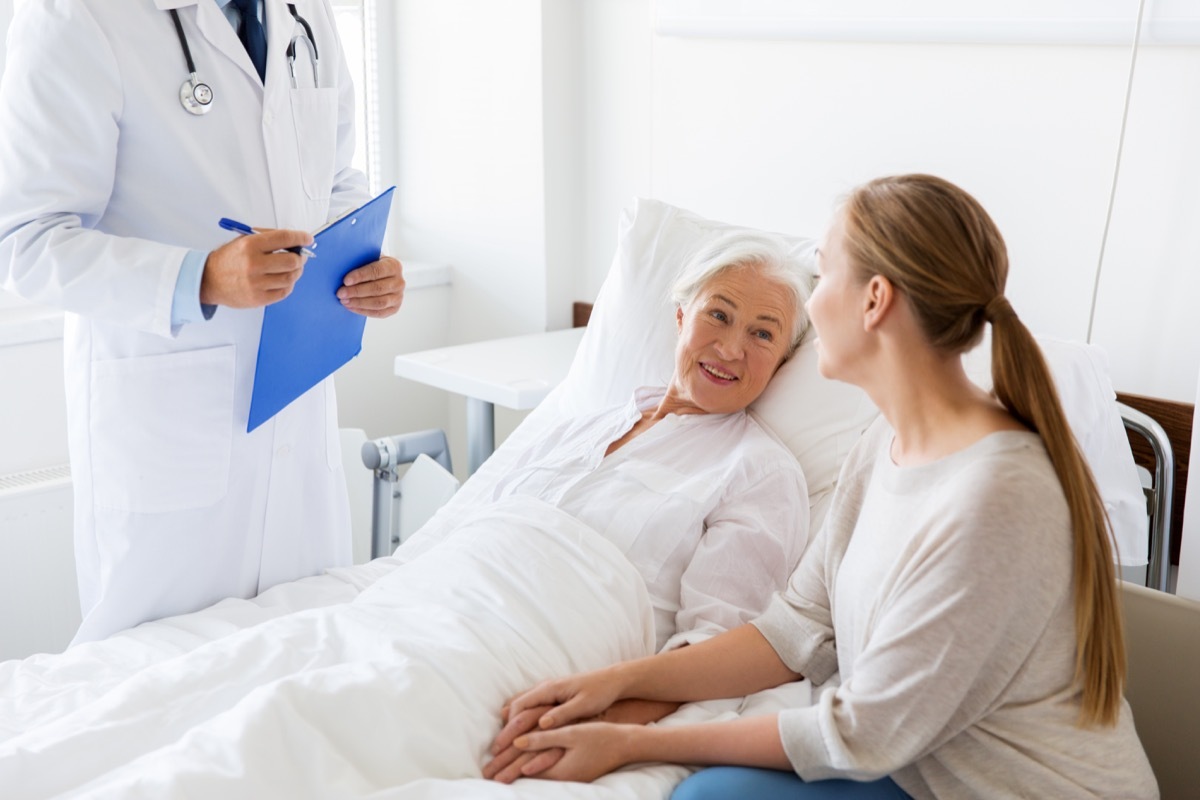 senior woman patient with daughter and doctor with clipboard at hospital ward