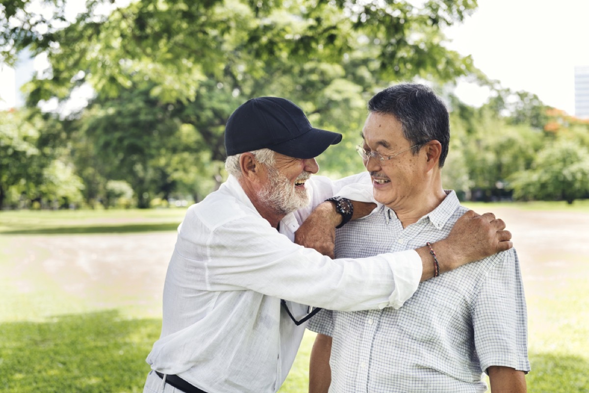 older white man embracing older asian man in park