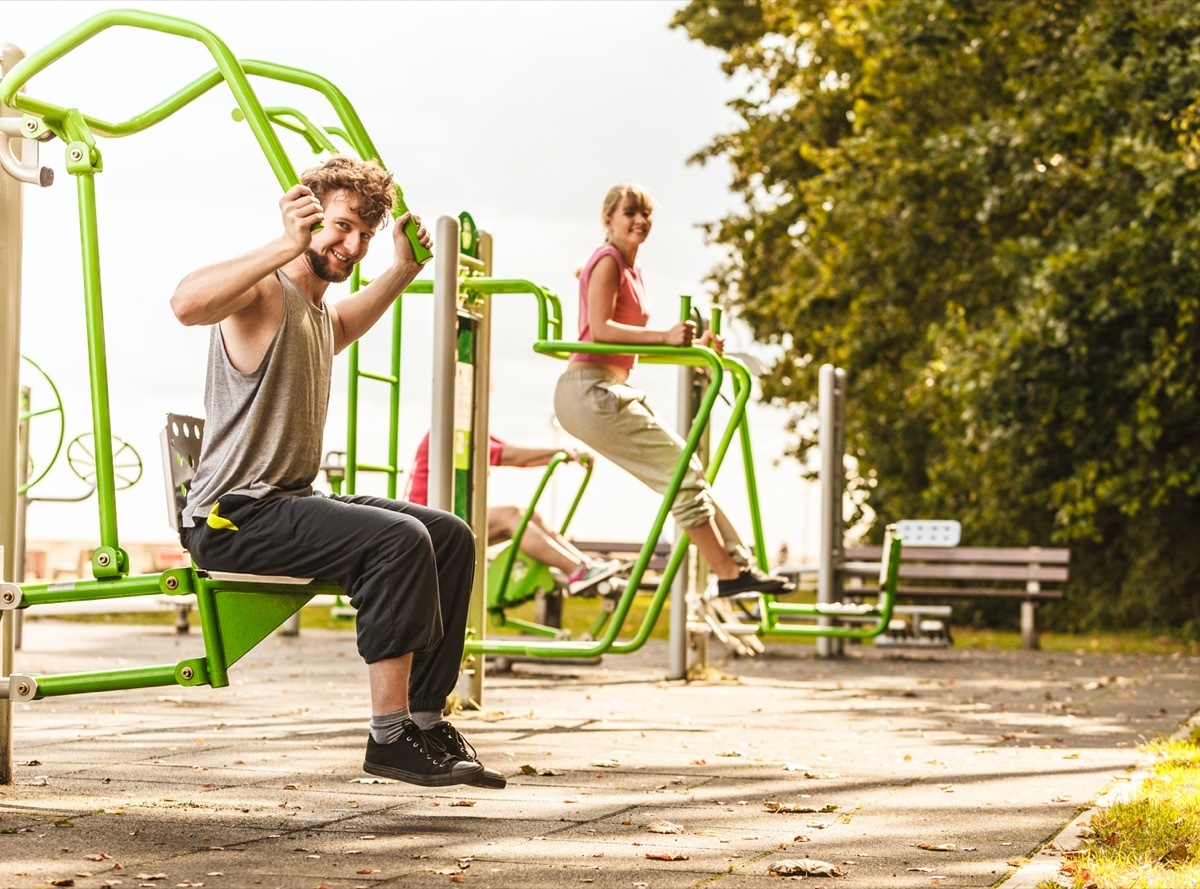 Muscular strong guy and girl in training suit working out at outdoor gym.